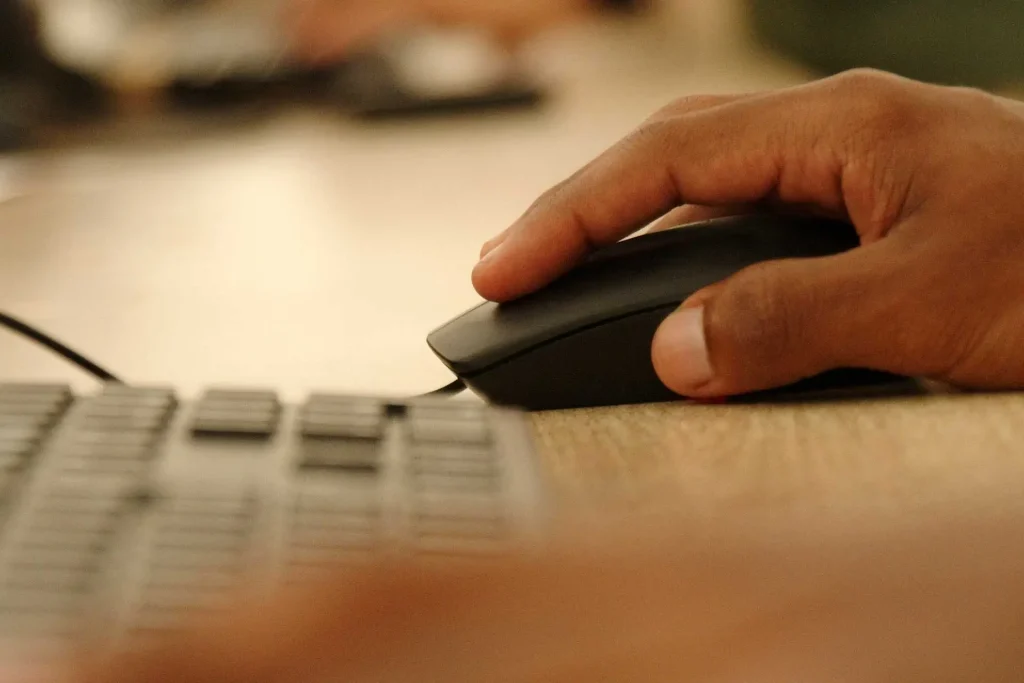 Mão segurando um mouse ao lado de um teclado, representando a necessidade de levar eletrônicos essenciais.